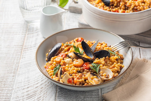 Fregola sarda con cozze disposta su un piatto fondo che poggia su un tavolo di legno.