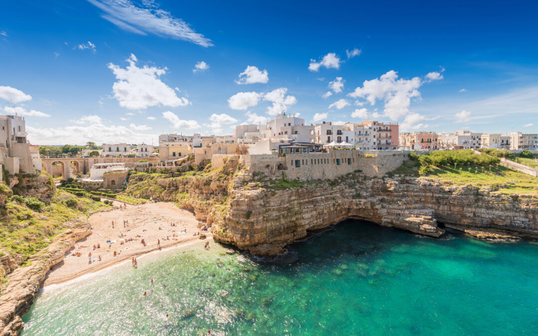 Blick auf Polignano a Mare: malerische weiße Häuser auf Klippen über dem türkisblauen Meer, mit einer kleinen Strandbucht darunter.