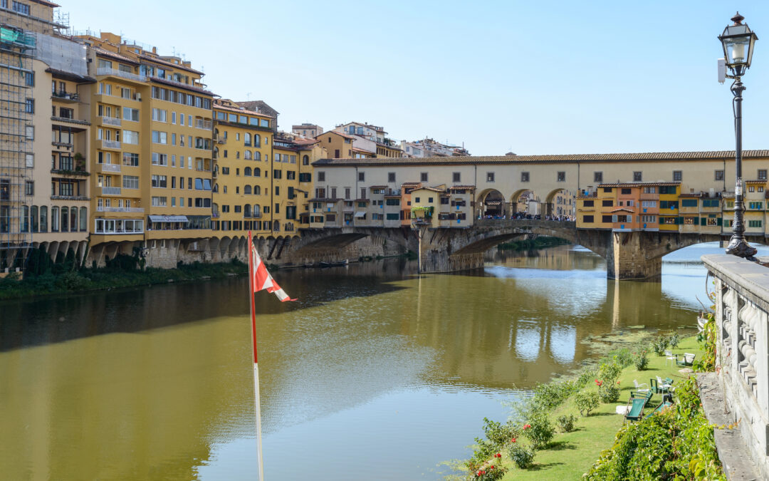 Der historische Ponte Vecchio in Florenz, gesäumt von goldenen Lichtreflexionen im Arno.