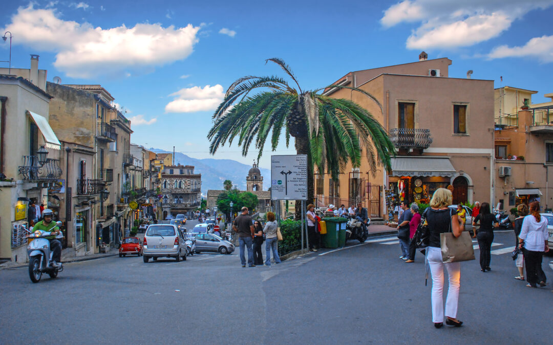 Ein Panoramablick auf Taormina mit dem griechischen Theater im Vordergrund und dem majestätischen Ätna im Hintergrund bei strahlendem Sonnenschein.