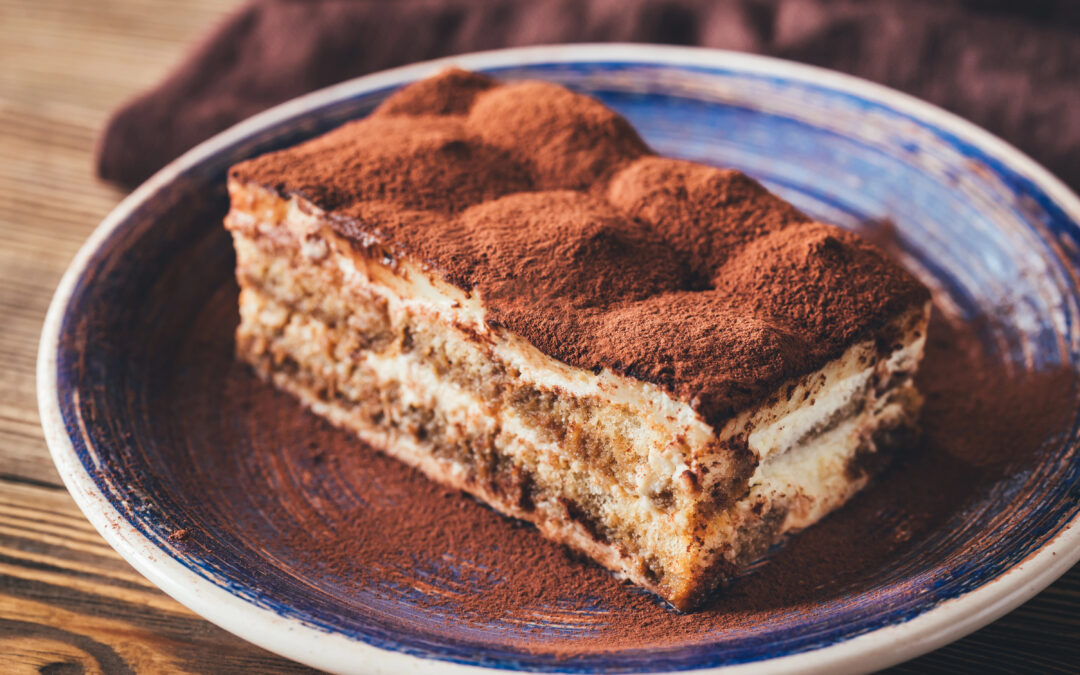 in Stück Tiramisu mit Mascarponecreme und Kakaopulver, serviert auf einem Teller.