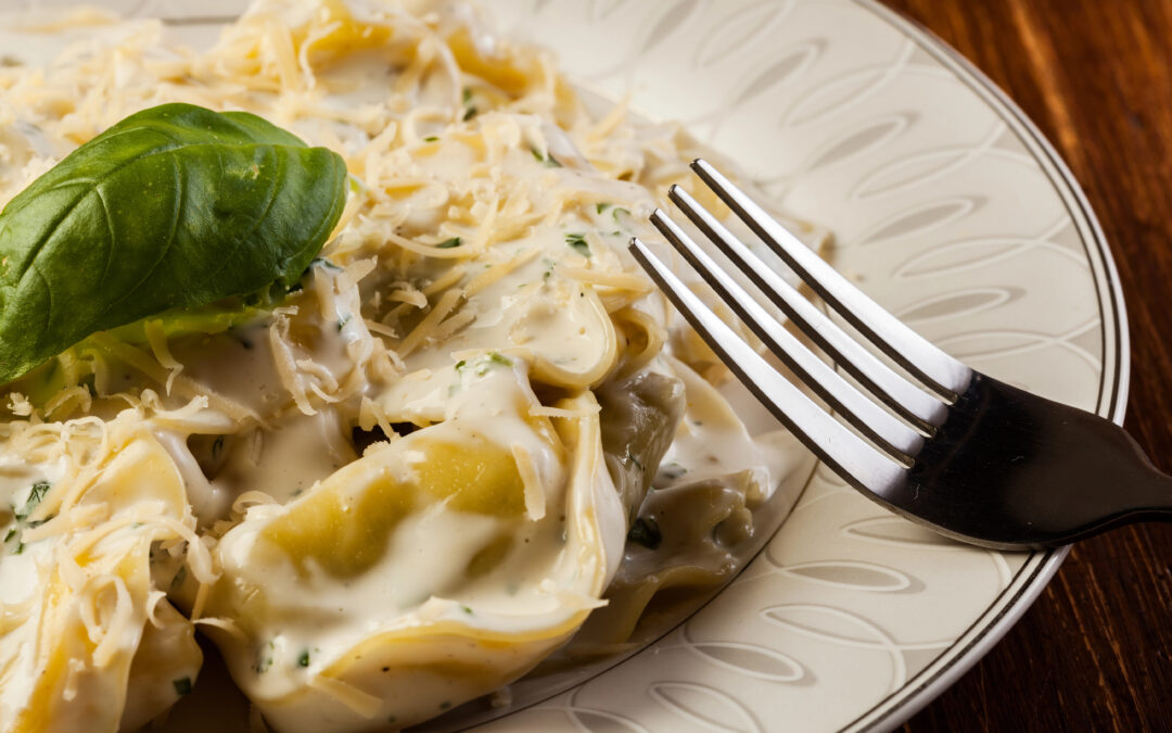 Nahaufnahme eines Tellers Tortellini alla panna: die gefüllten Teigtaschen in einer cremigen, weißen Sauce, garniert mit Parmesan.