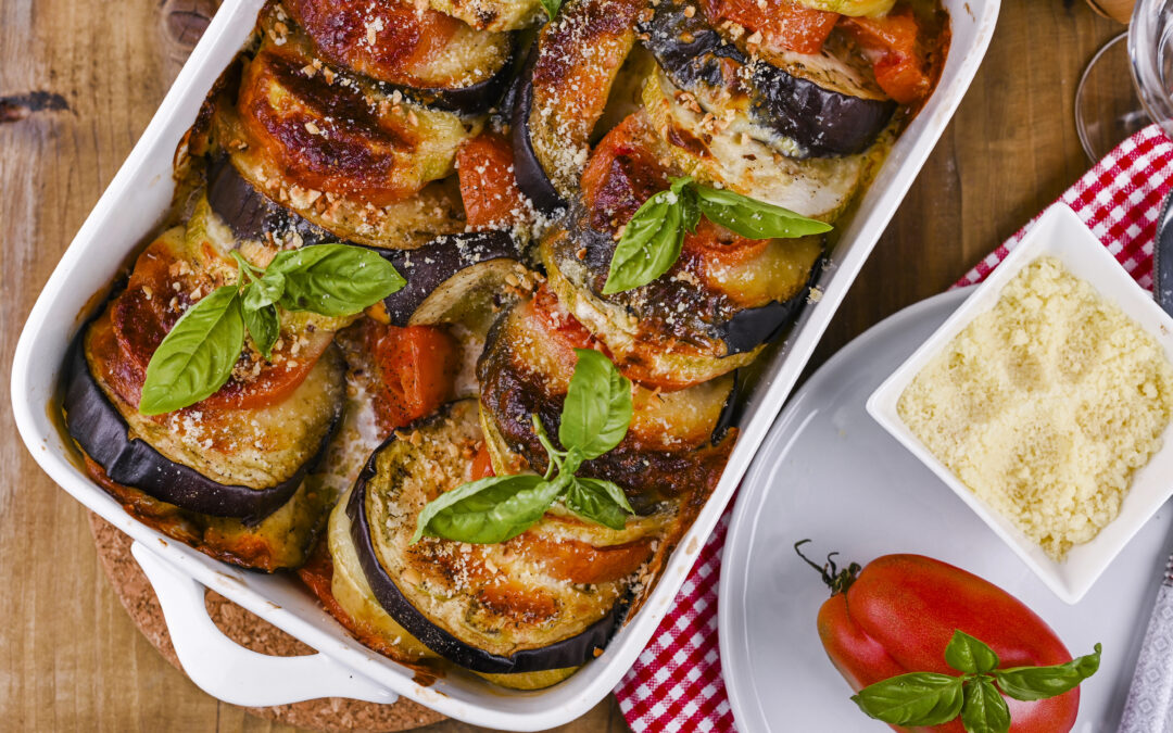 Vogelperspektive auf eine Auflaufform mit Parmigiana: Schichtweise angeordnete frittierte Auberginenscheiben, überzogen mit Tomatensauce und geschmolzenem Käse.