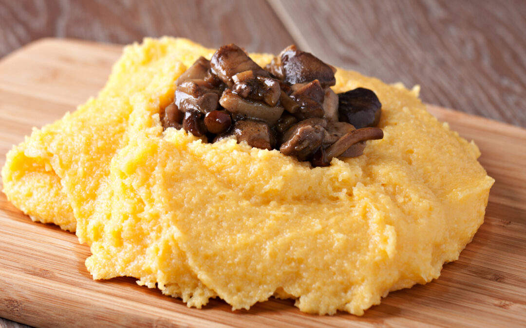 Ein Teller cremige Polenta, garniert mit Parmesan und Butter, serviert als Beilage zu einem herzhaften Gericht.