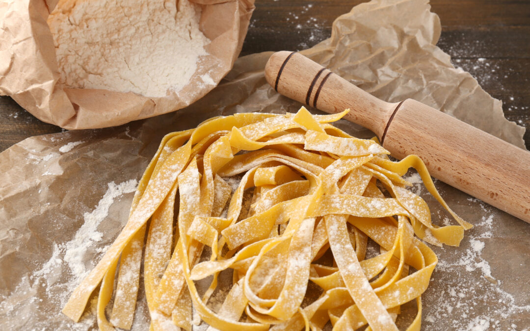 Nahaufnahme von frischen Eier-Tagliatelle, die sorgfältig auf einer Holzoberfläche ausgebreitet sind, bereit zum Schneiden oder Kochen.