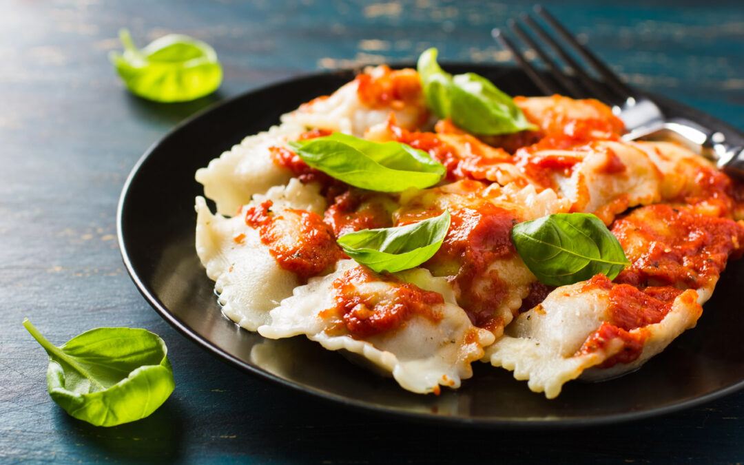 Teller mit frischen Ravioli in Tomatensauce, garniert mit Basilikum, in Nahaufnahme.